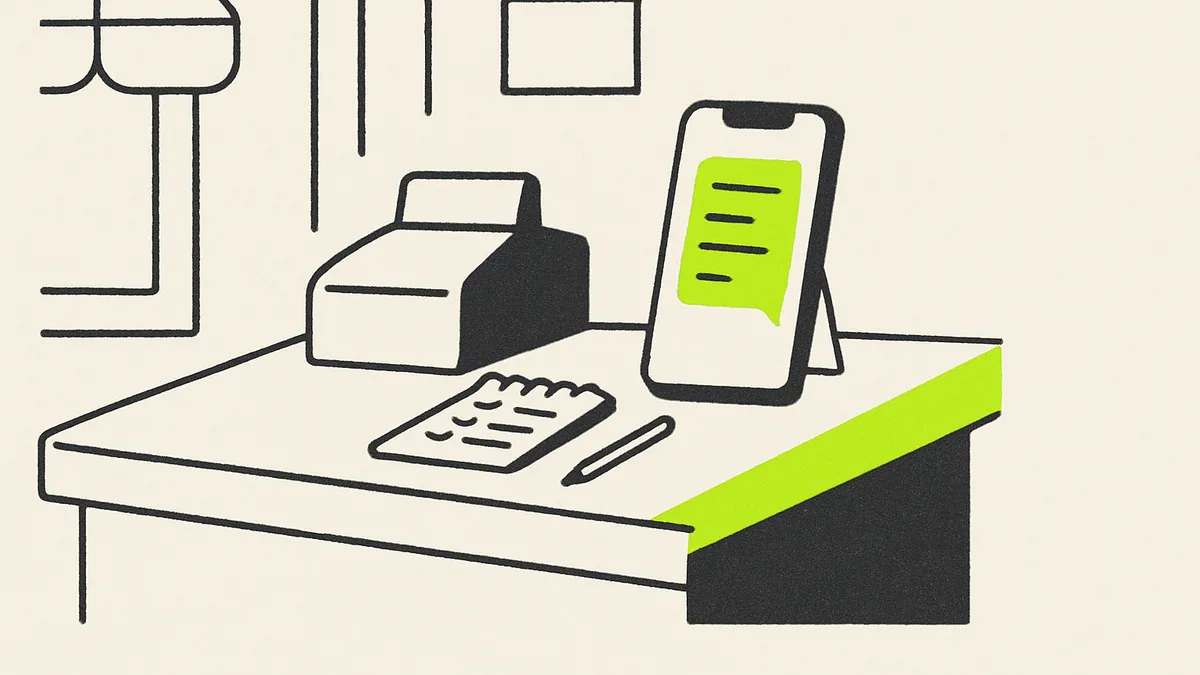 A smartphone propped on a shop counter showing a simple chat screen, with a notepad and a coffee cup beside it.